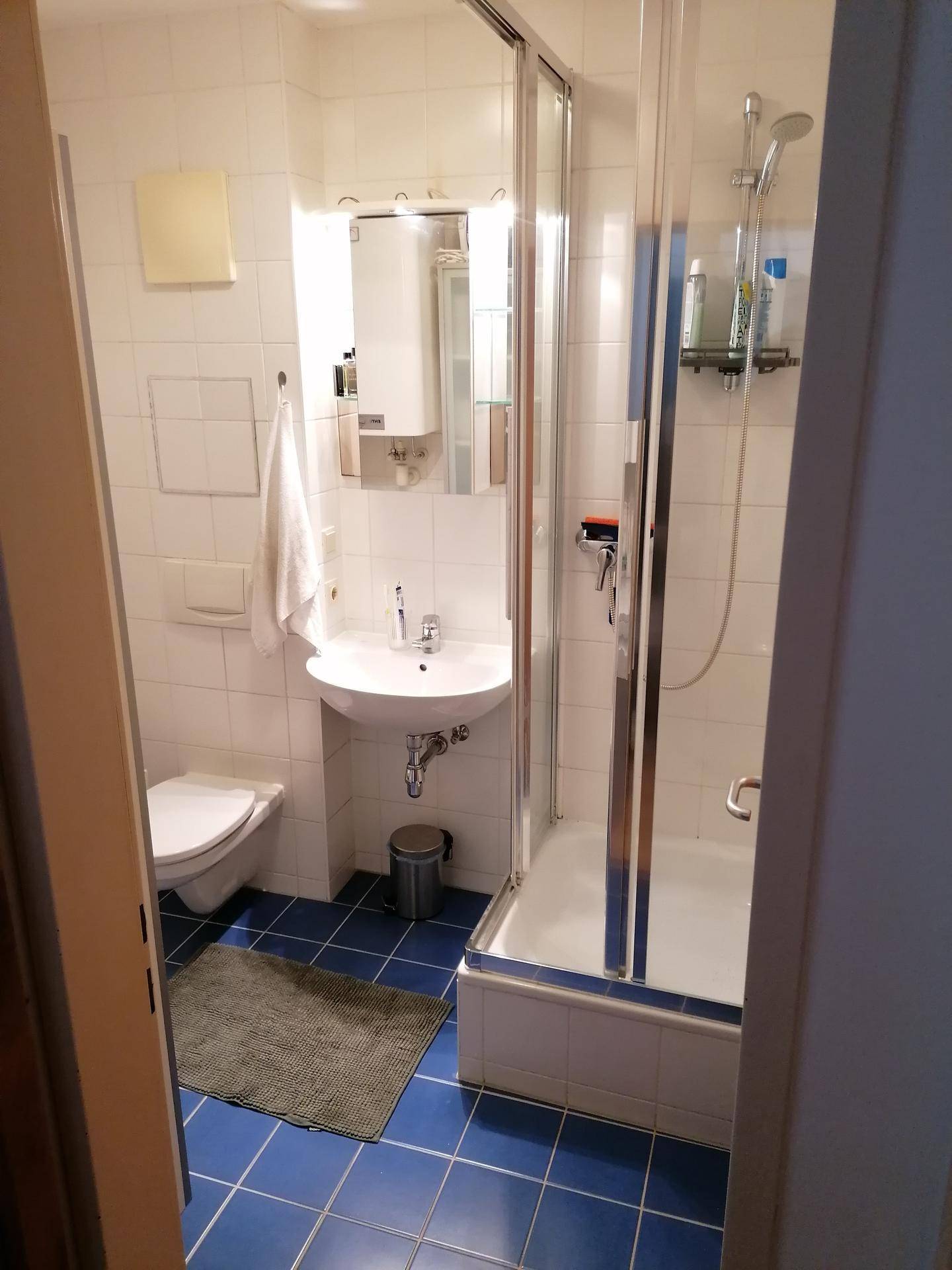 Kleines Badezimmer mit Duschkabine, WC und Waschbecken, ausgestattet mit blauen Bodenfliesen.