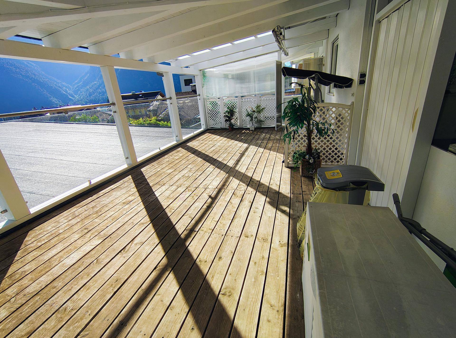 Große Holzterrasse mit weitem Blick auf die umliegende Berglandschaft und viel Sonne.