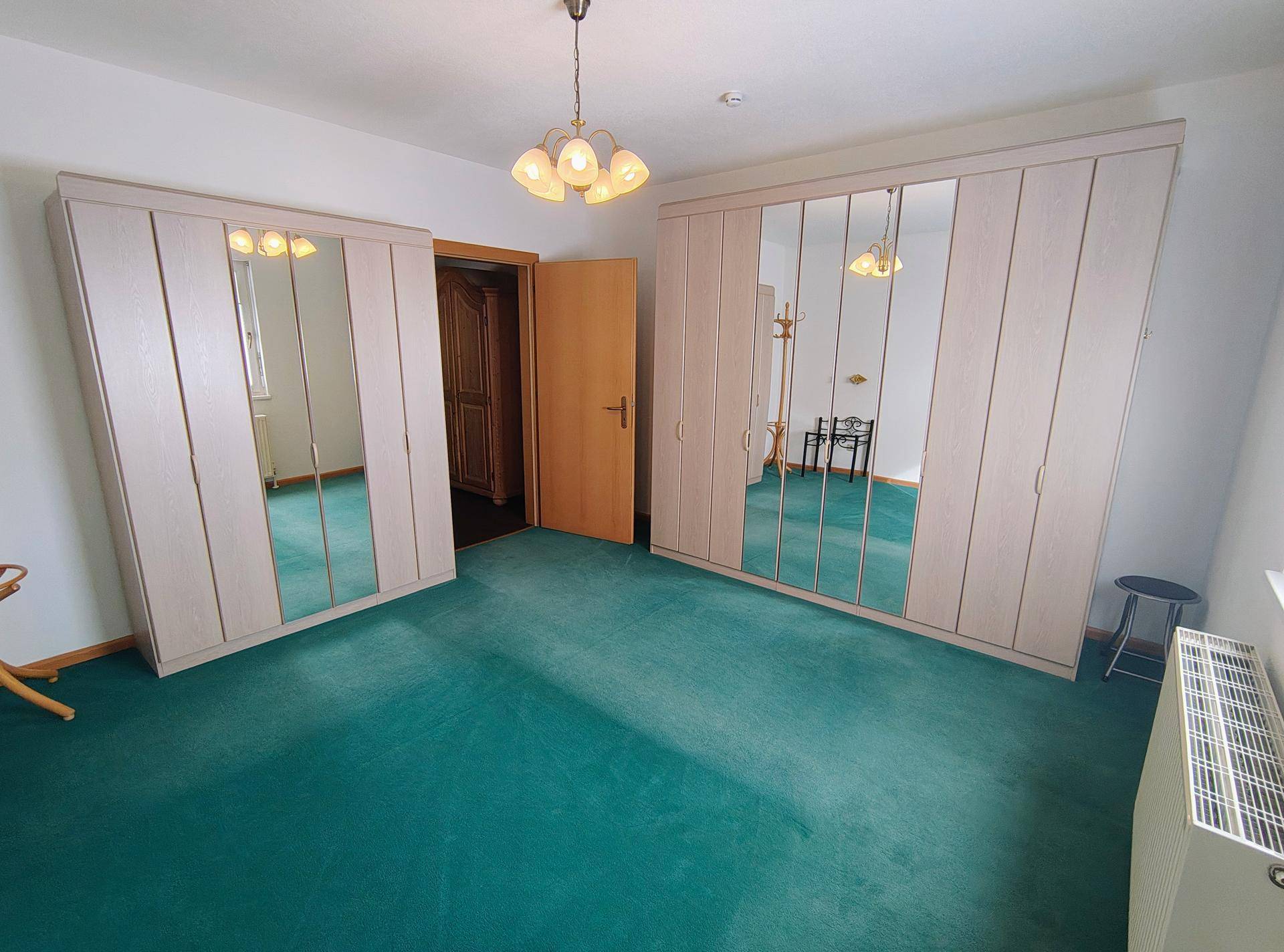 Schlafzimmer mit grünem Teppichboden und großen Spiegelschränken für viel Stauraum.