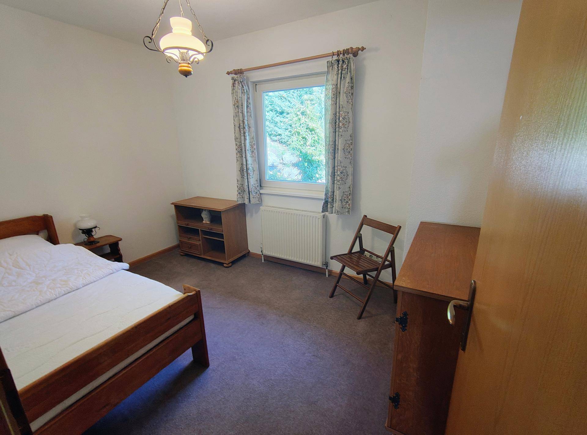 Gemütliches Schlafzimmer mit Einzelbett, Holzmöbeln und Blick ins Grüne.
