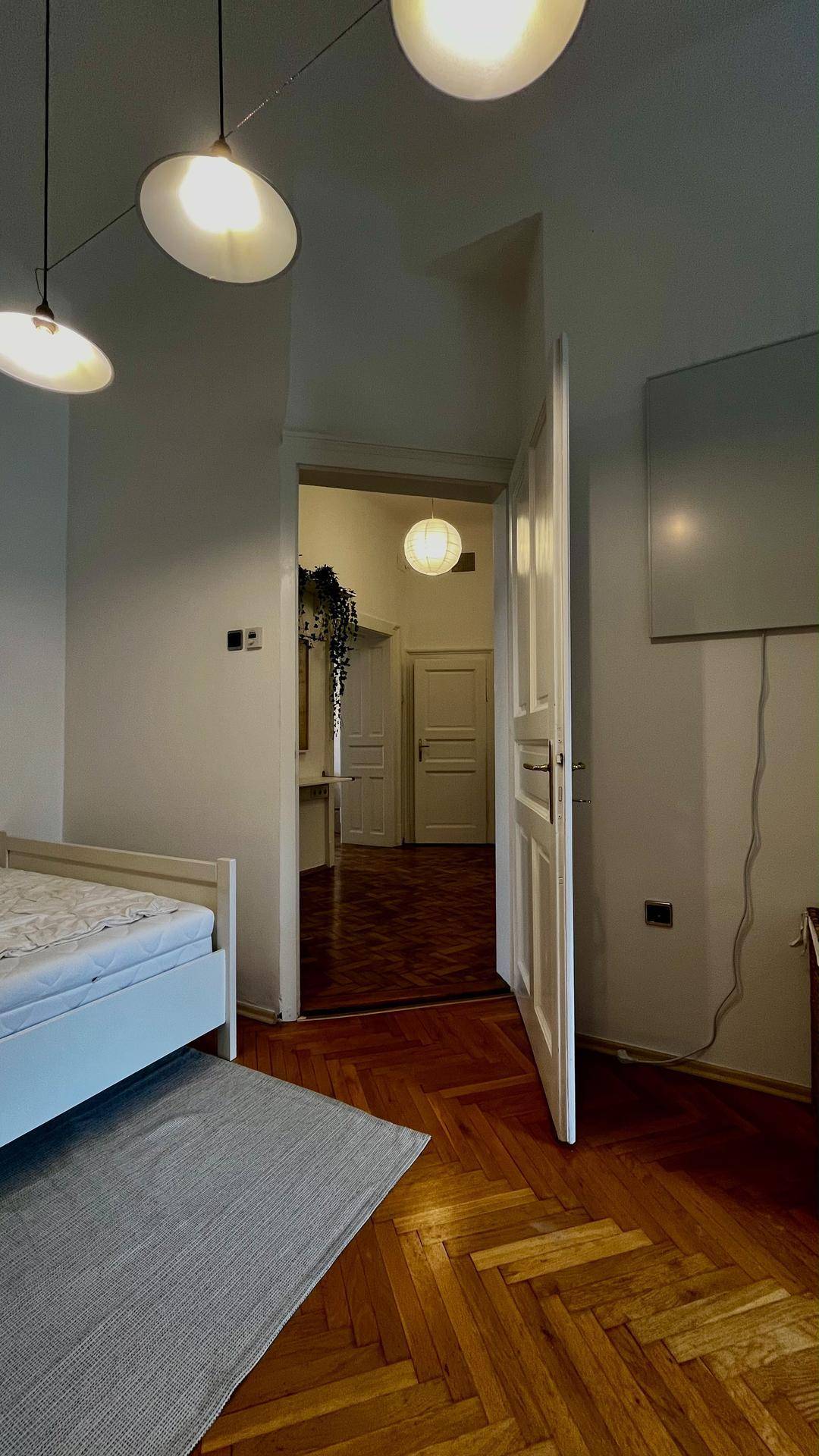 Schlafzimmer mit Holzboden, modernem Bett und Blick in den angrenzenden Flur.