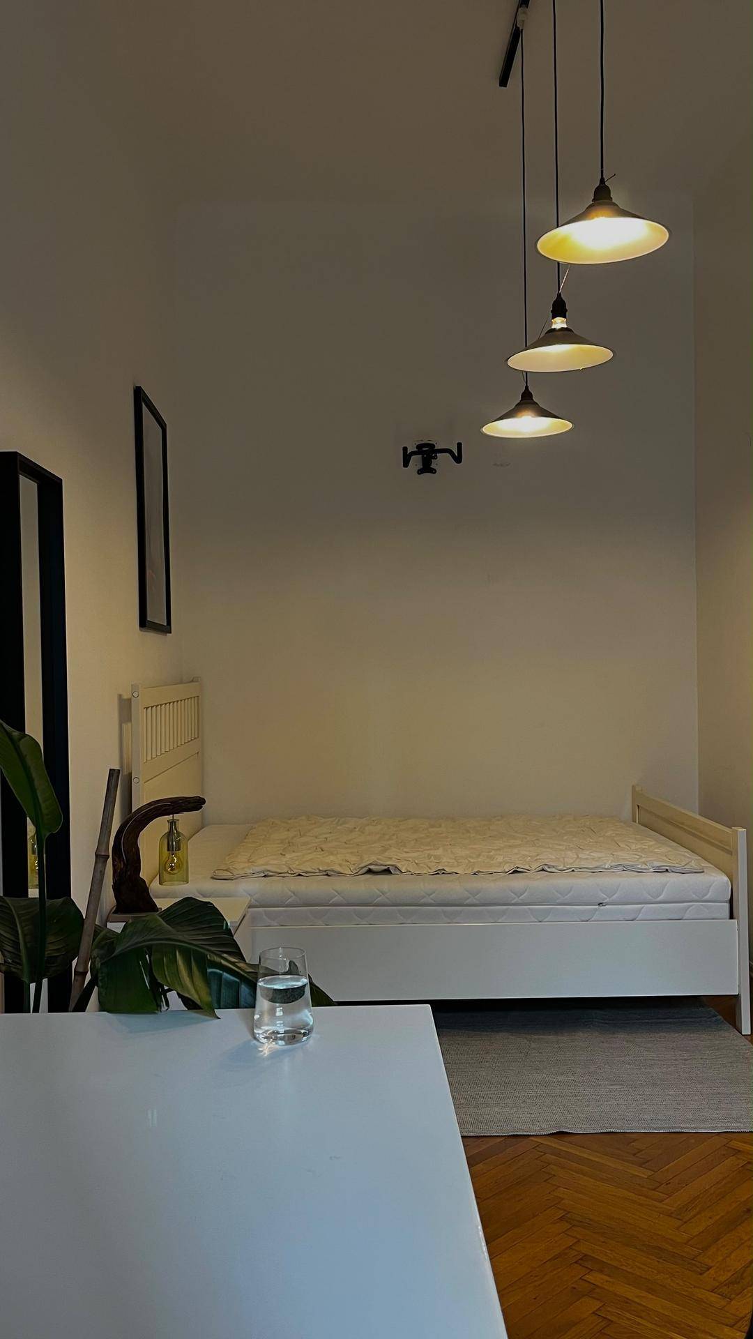 Schlafzimmer mit Holzboden, weißem Bettrahmen und minimalistischer Einrichtung.