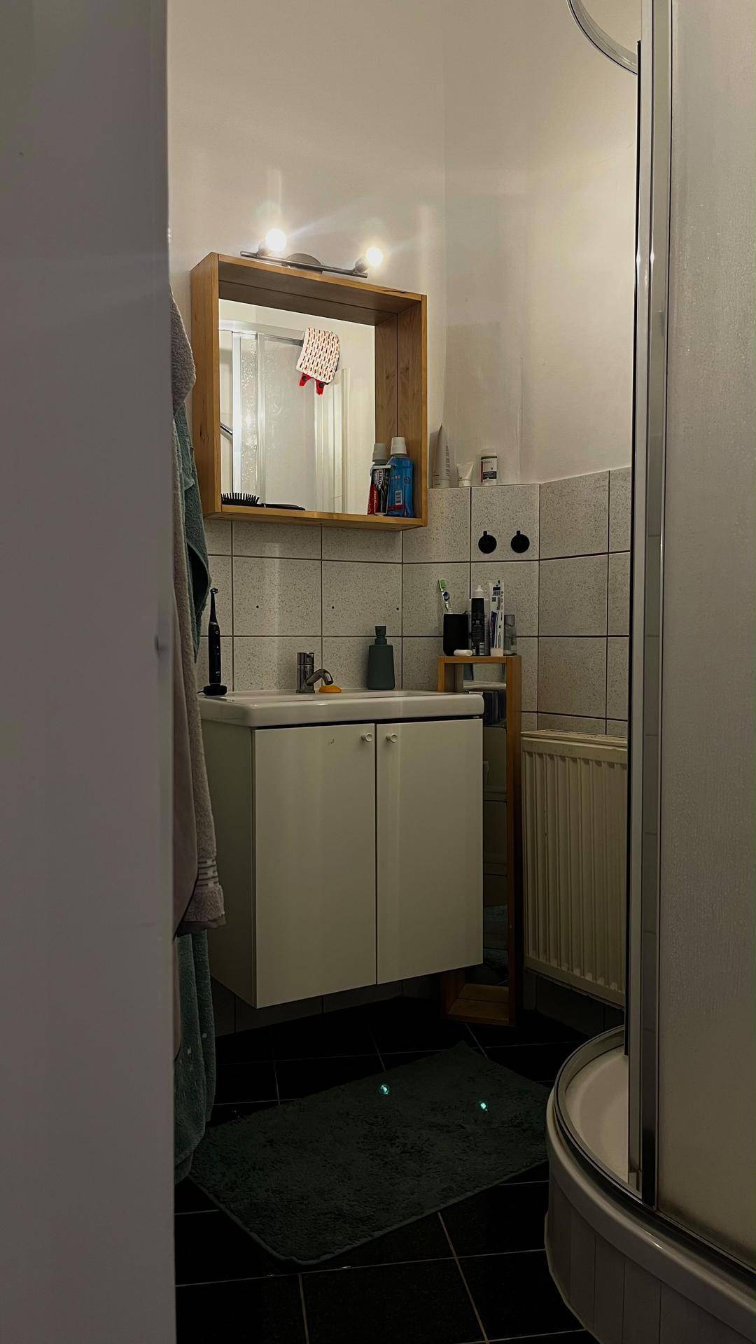 Kleines Badezimmer mit Duschkabine, Waschbecken und Spiegelschrank.