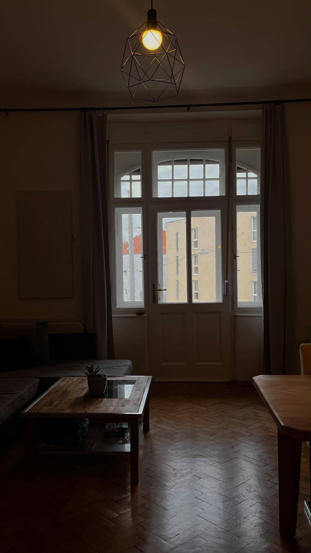 Wohnzimmer mit Holzboden, Couch und großen Fenstertüren, die viel Licht hereinlassen.