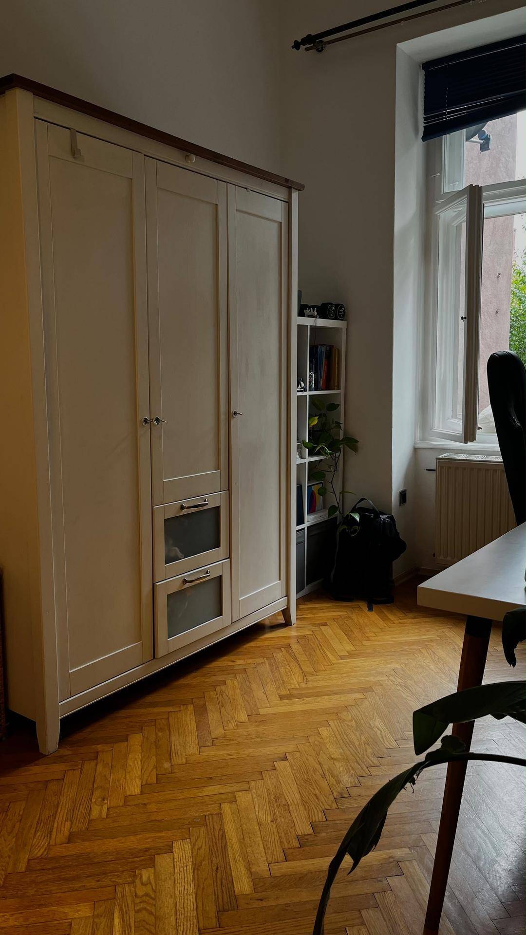 Heller Raum mit Holzboden, großem Kleiderschrank und Fenster mit Blick ins Grüne.