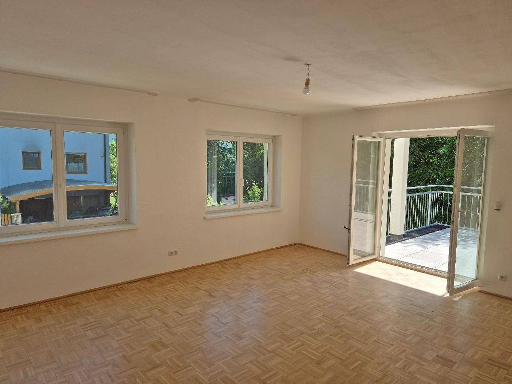Geräumiges, leeres Zimmer mit Parkettboden, großen Fenstern und direktem Zugang zu einem sonnigen Balkon.