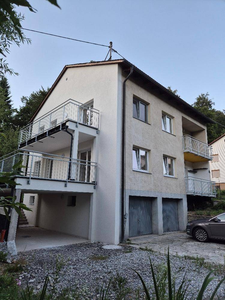 Mehrstöckiges Wohnhaus mit mehreren Balkonen und Garagen, eingebettet in eine grüne Umgebung.