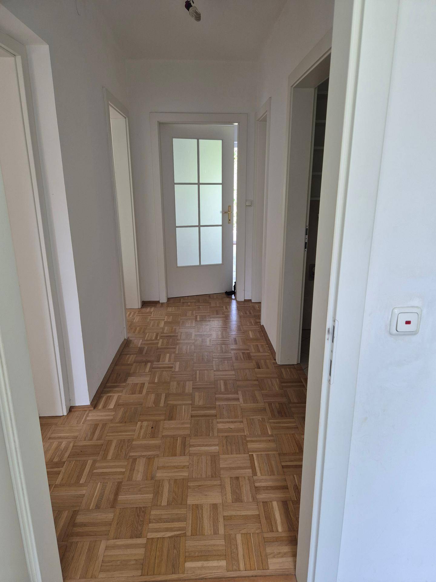 Heller Flur mit klassischem Parkettboden, weißen Wänden und Türen zu angrenzenden Räumen.