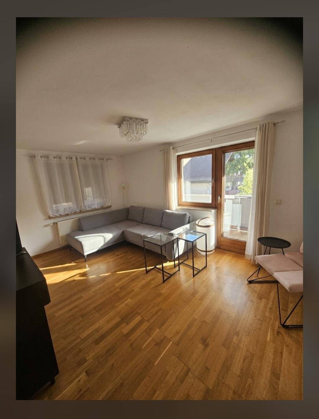 Helles Wohnzimmer mit Parkettboden, gemütlichem Sofa und Zugang zu einem kleinen Balkon.