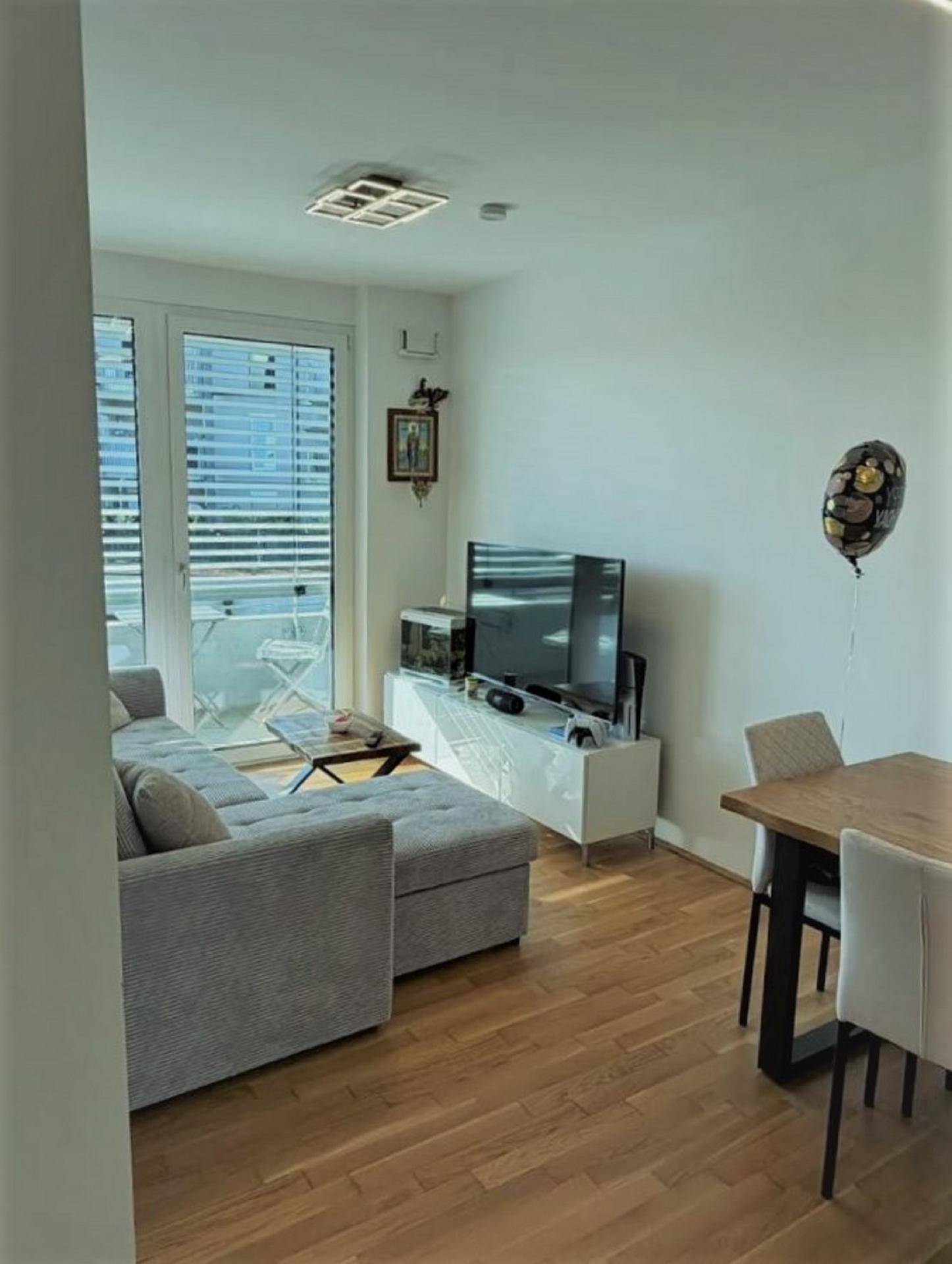 Lichtdurchfluteter Wohn- und Essbereich mit Parkettboden, Sofa und Zugang zu einem Balkon.
