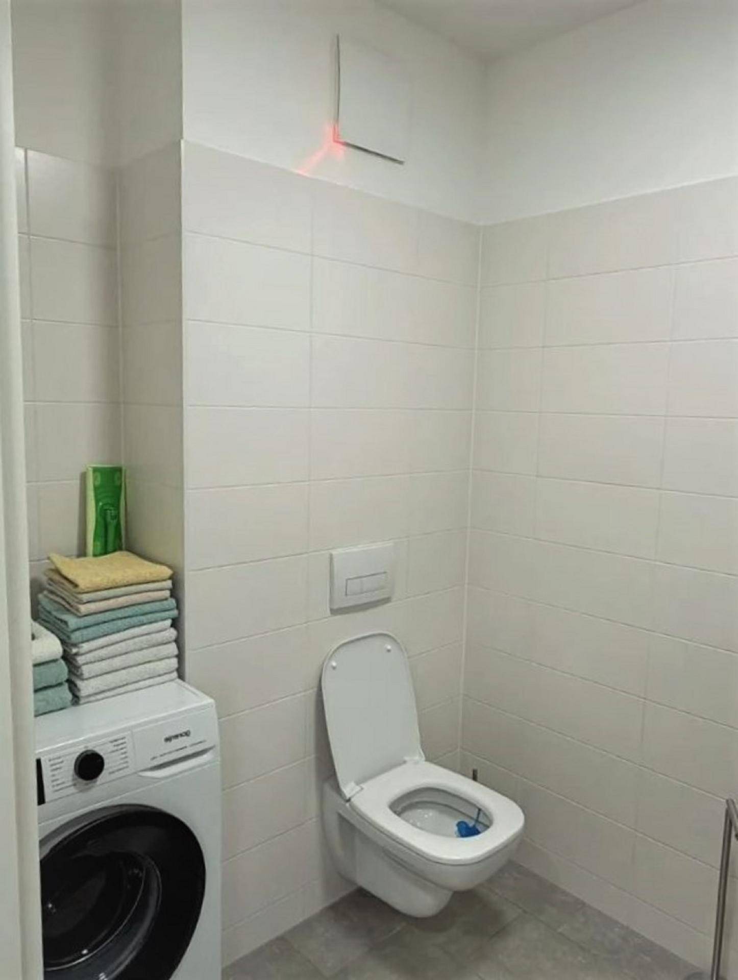 Separates WC mit wandhängender Toilette, weißen Fliesen und einer praktischen Waschmaschine.