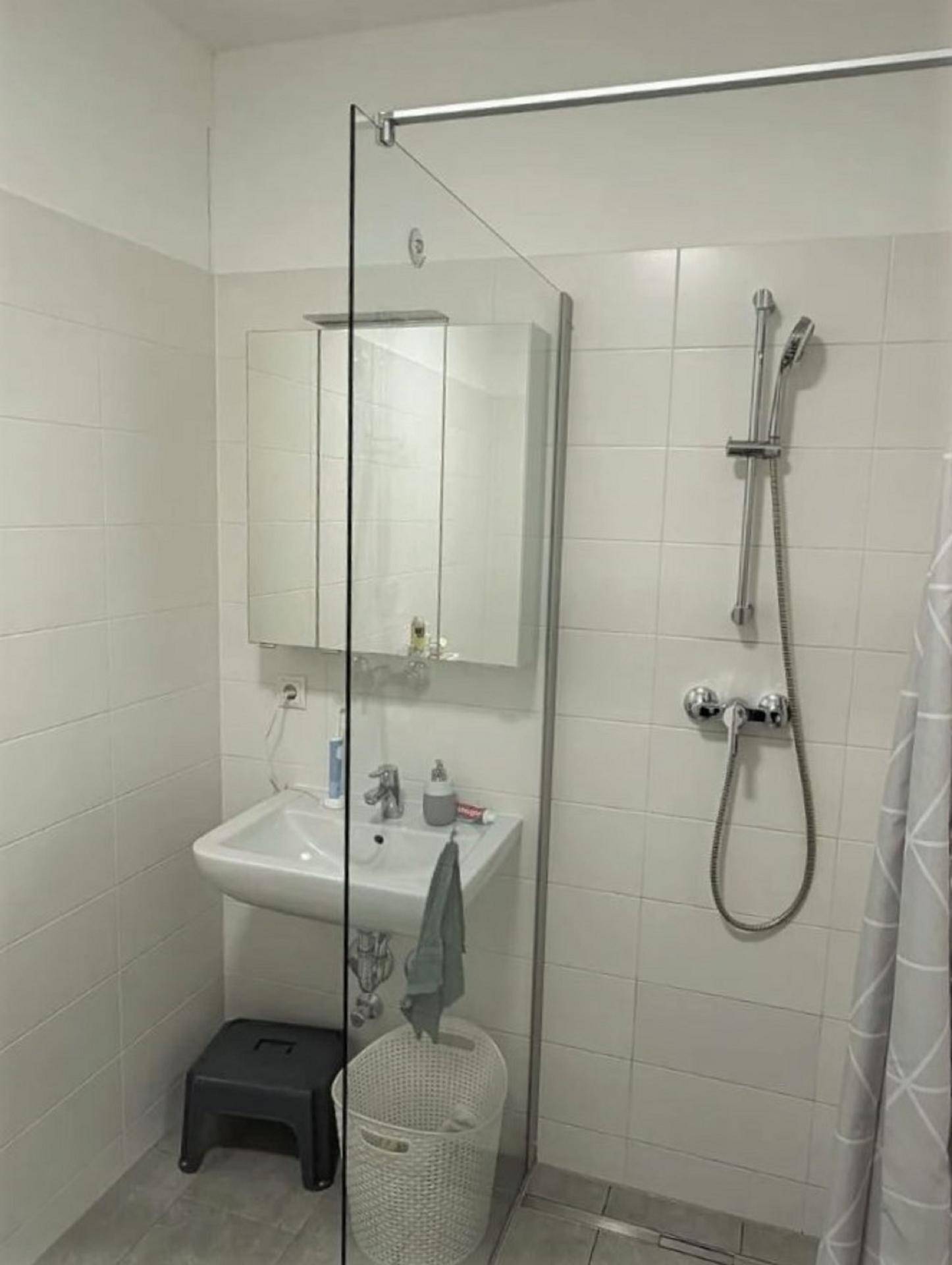 Helles Badezimmer mit einer Duschkabine, Waschbecken, Spiegelschrank und weißen Wandfliesen.