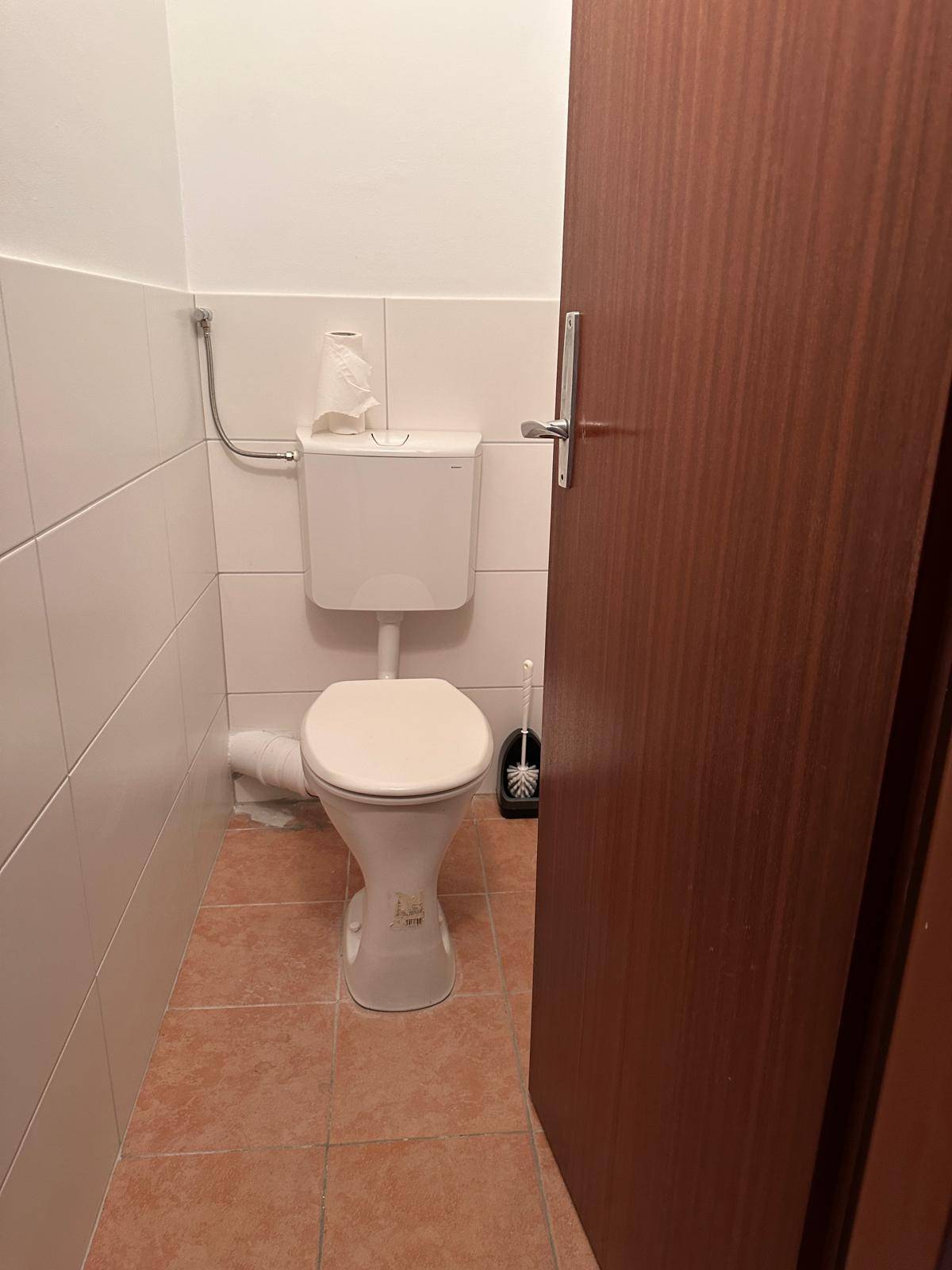 Separates WC mit weißen Fliesen und Terrakotta-Bodenfliesen, sauber und funktional.