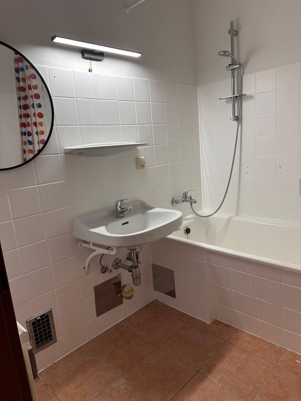 Badezimmer mit weißen Fliesen, Waschbecken und Badewanne mit Duschfunktion.