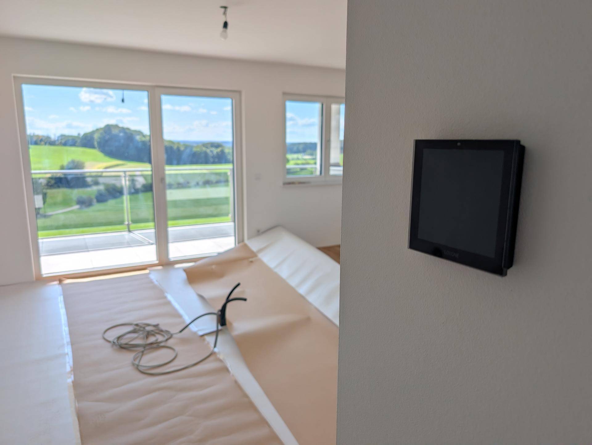 Wohnbereich mit großem Fenster, Balkonzugang und Blick auf die grüne Landschaft.