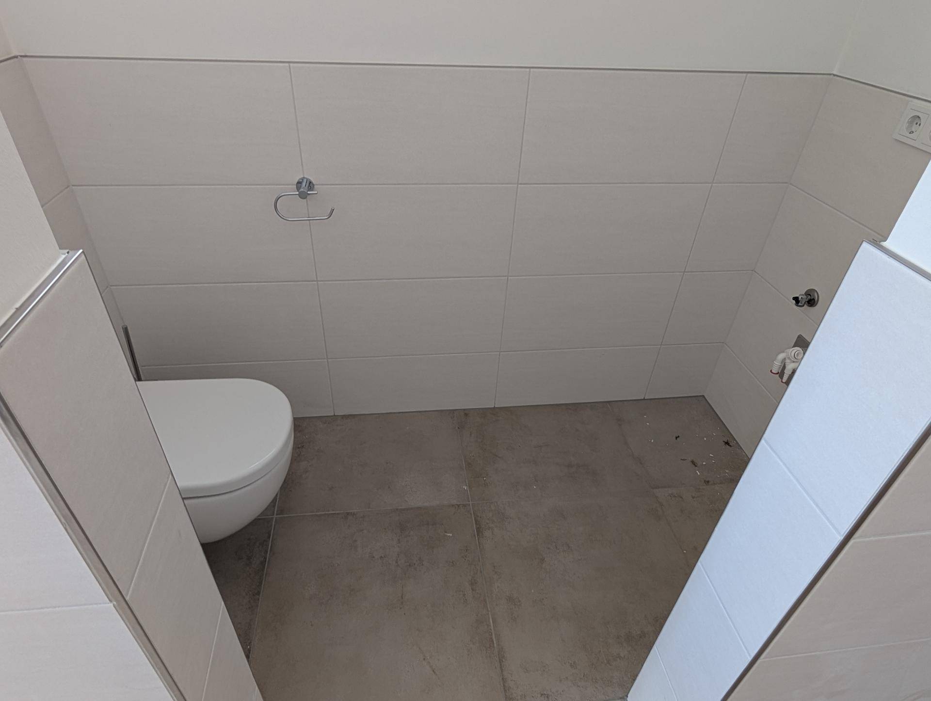 Modernes Gäste-WC mit wandmontierter Toilette und hellen Fliesen an den Wänden.