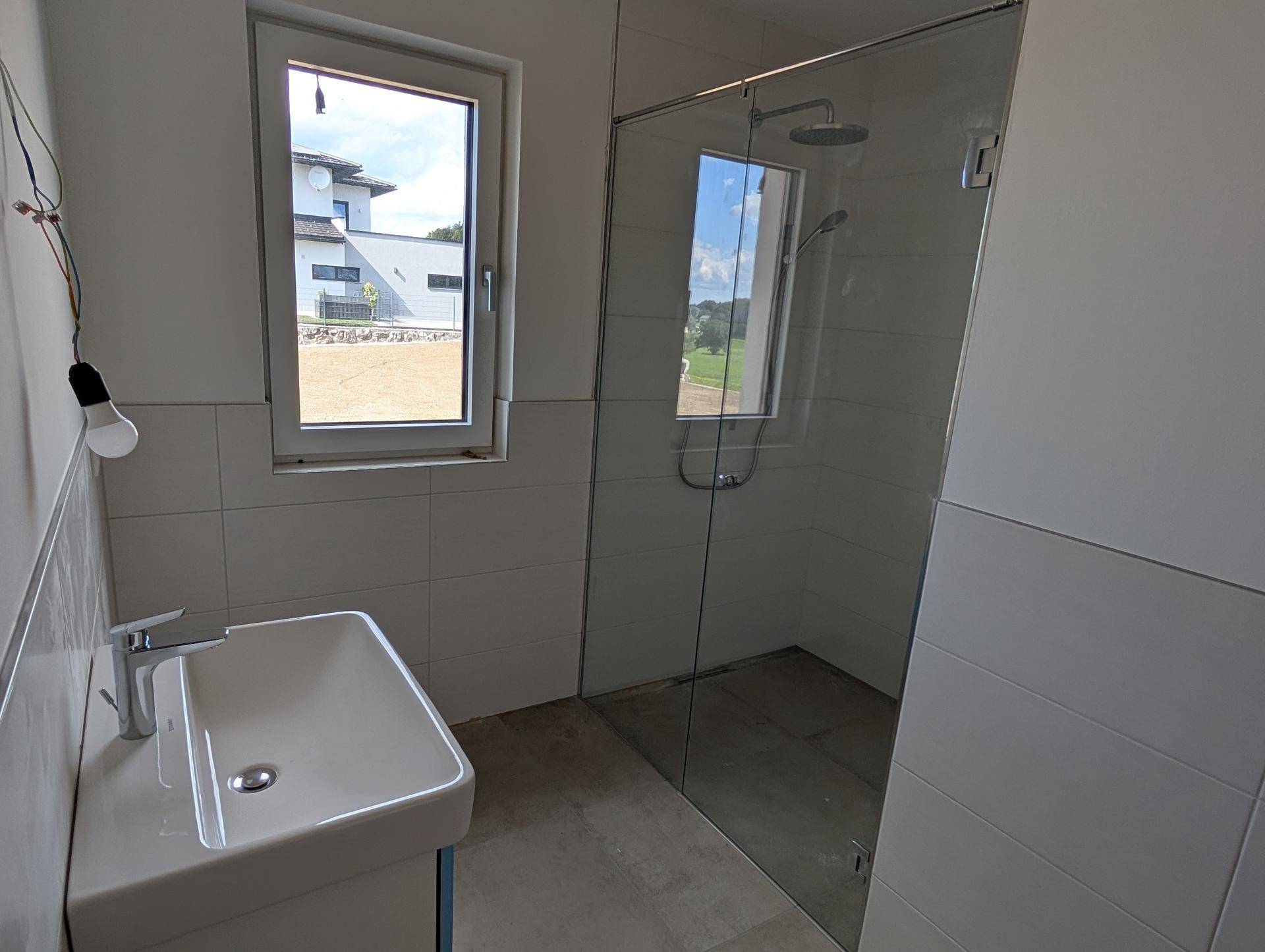 Helles Badezimmer mit moderner Dusche, Einzelwaschbecken und Fenster.