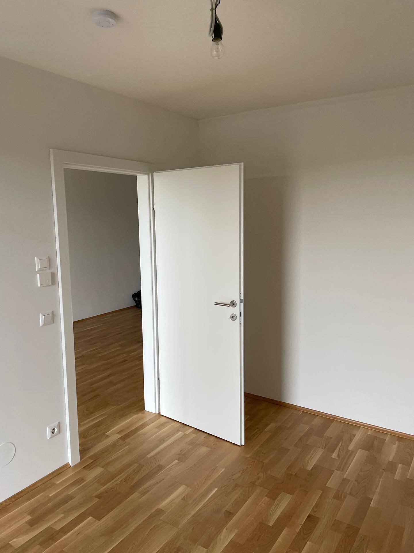 Heller Innenraum mit Parkettboden und einer offenen Tür, die den Blick in einen weiteren Raum freigibt.