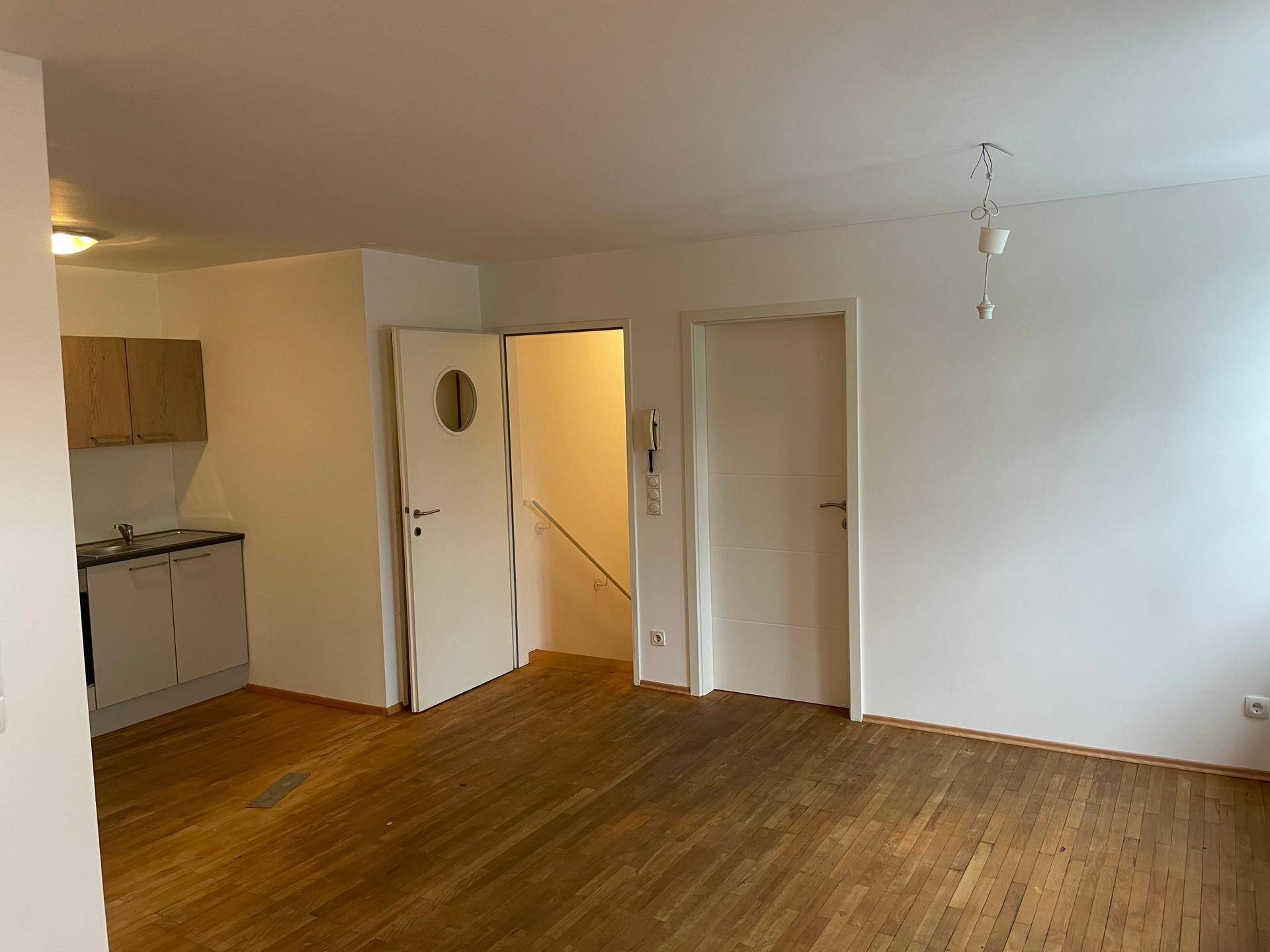 Offener Wohnbereich mit integrierter Küchenzeile, Holzparkettboden und Zugang zu weiteren Räumen.