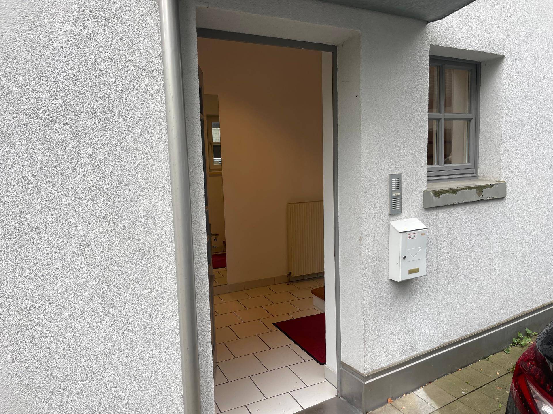 Eingangsbereich eines Gebäudes mit Briefkasten, Gegensprechanlage und einem kleinen Fenster.