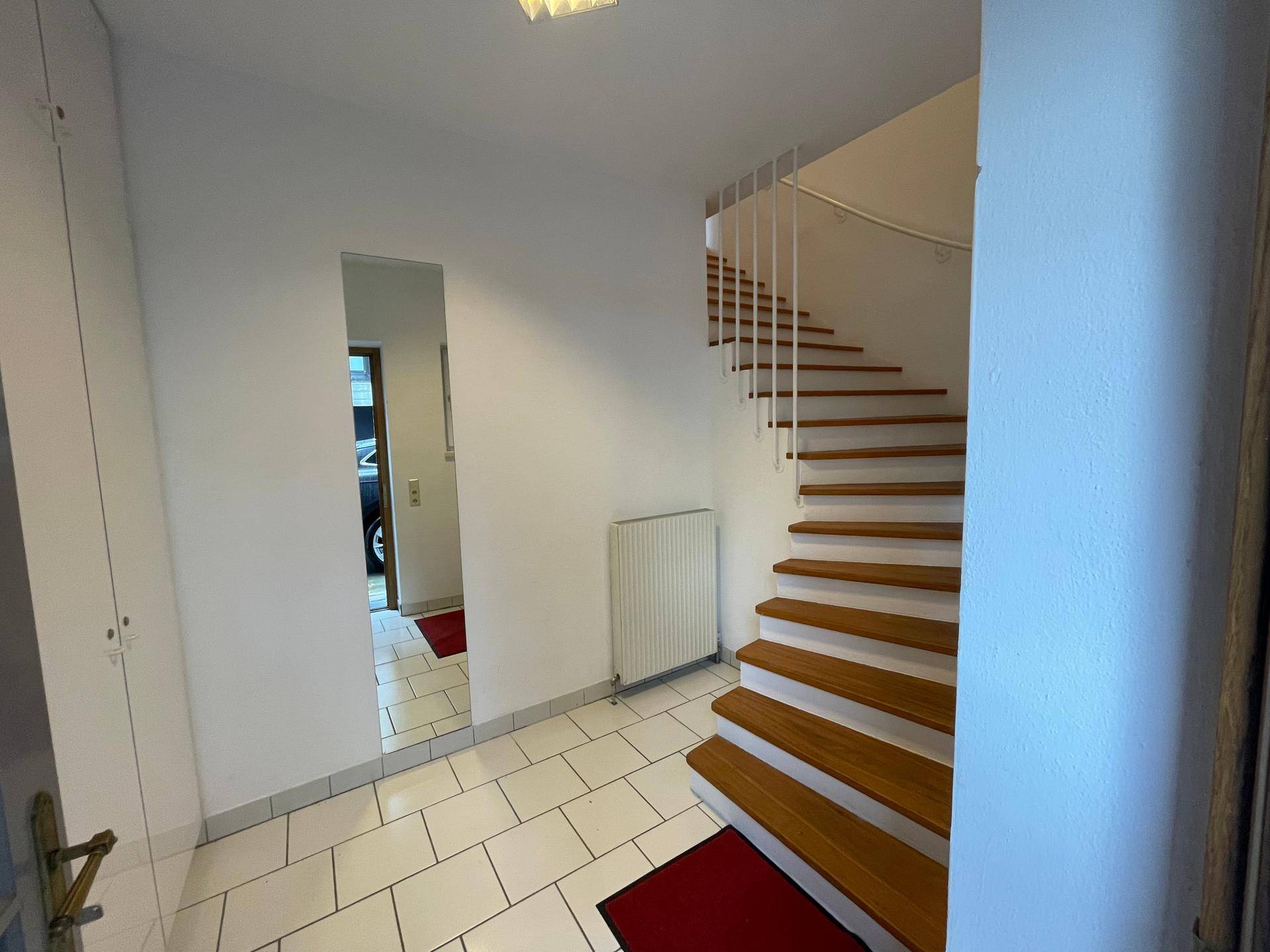 Heller Flur mit Fliesenboden, Holztreppe und großem Spiegel, führt zu den oberen Etagen.