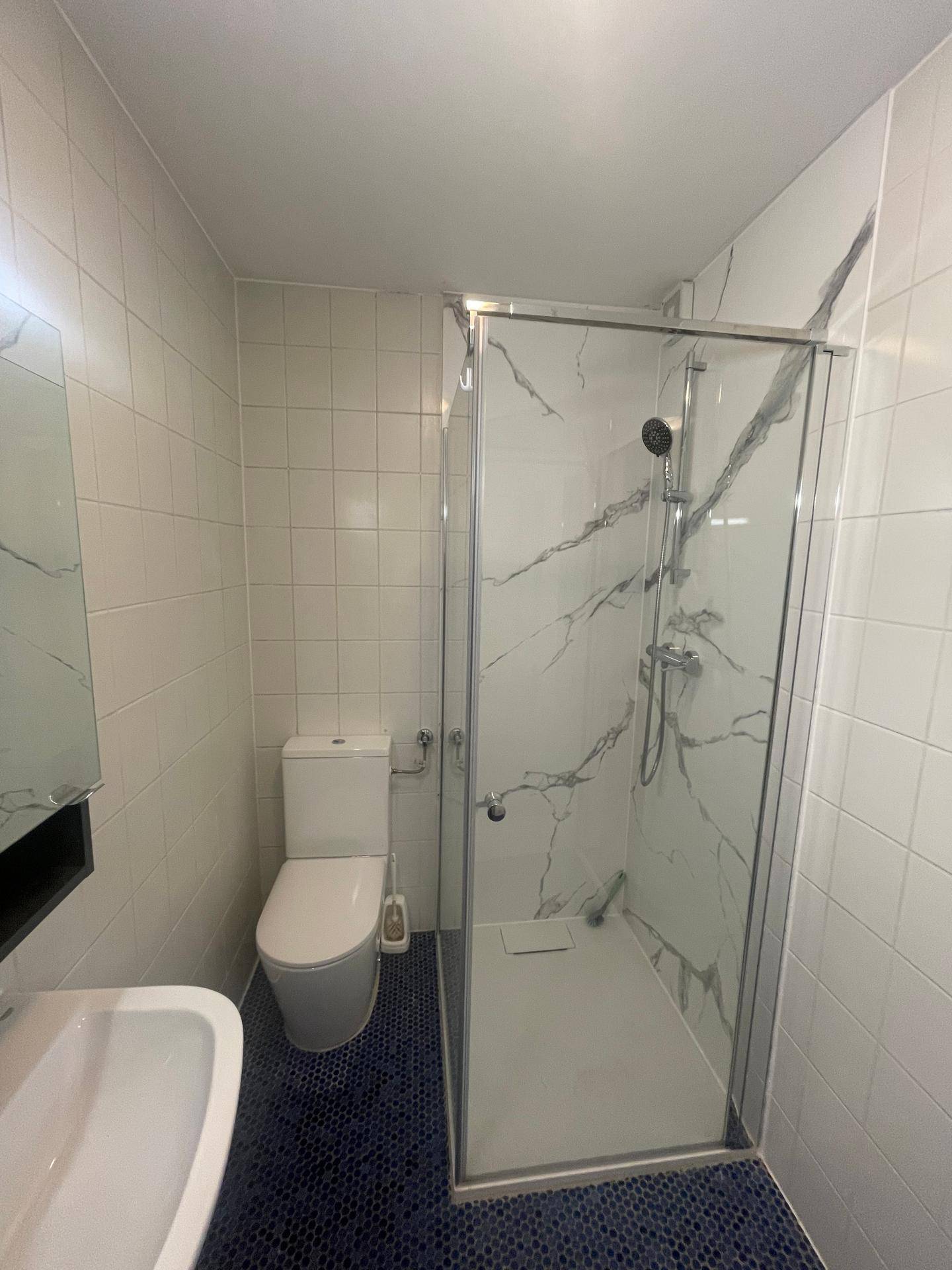 Modernes Badezimmer mit weißen Fliesen, begehbarer Dusche und dunklem Mosaikboden.