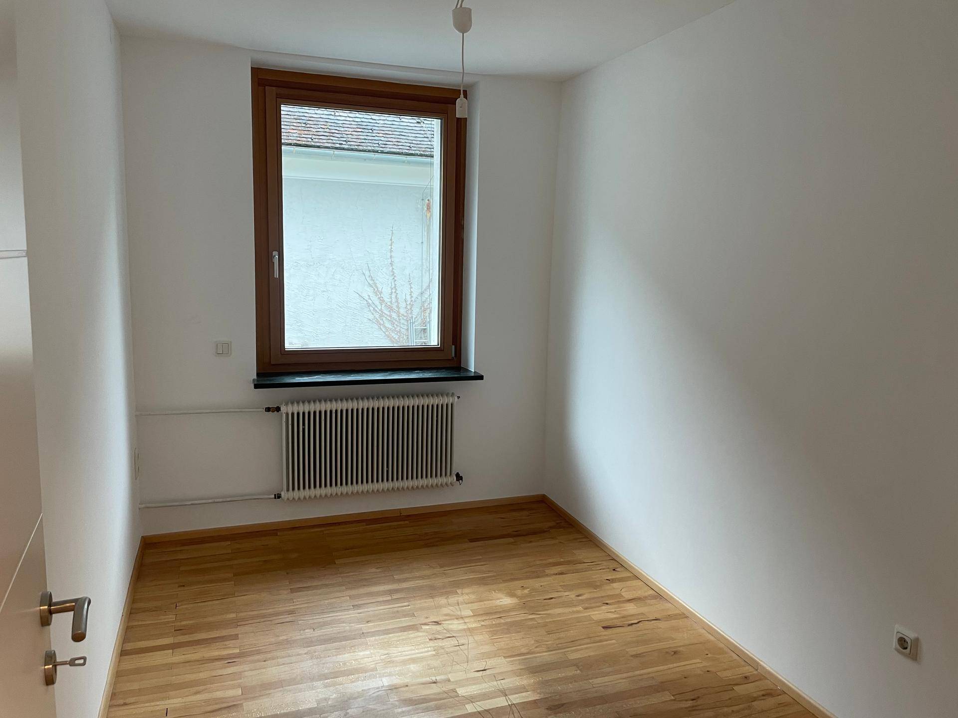 Gemütliches Zimmer mit Holzfenster, Heizkörper und Parkettboden, ideal als Schlaf- oder Arbeitszimmer.