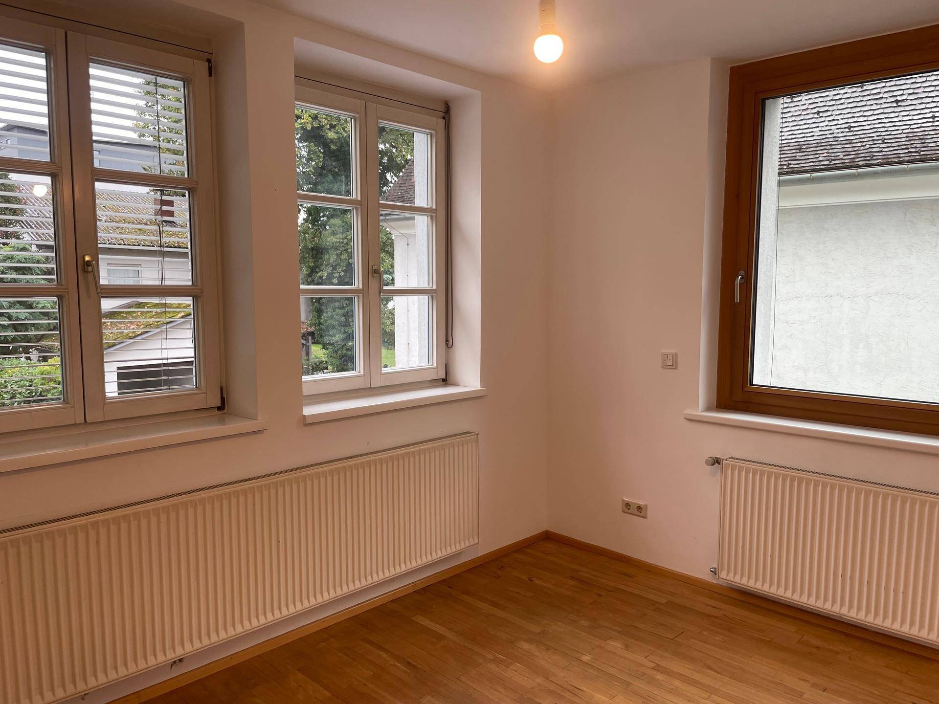 Heller Raum mit zwei großen Fenstern, Parkettboden und Heizkörpern, bietet viel Tageslicht.