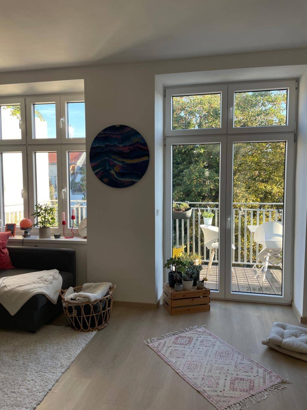 Helles Wohnzimmer mit Holzboden, großzügigen Fenstern und Zugang zu einem möblierten Balkon.