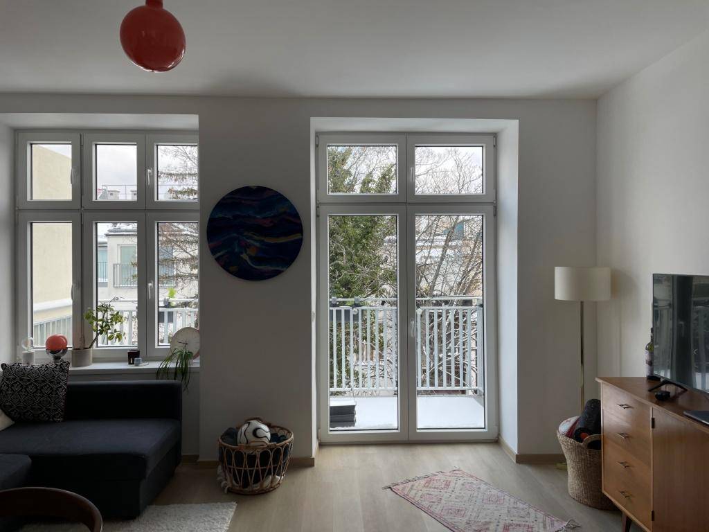 Helles Wohnzimmer mit Sofa, Sideboard und Balkonzugang, Blick auf winterliche Bäume.
