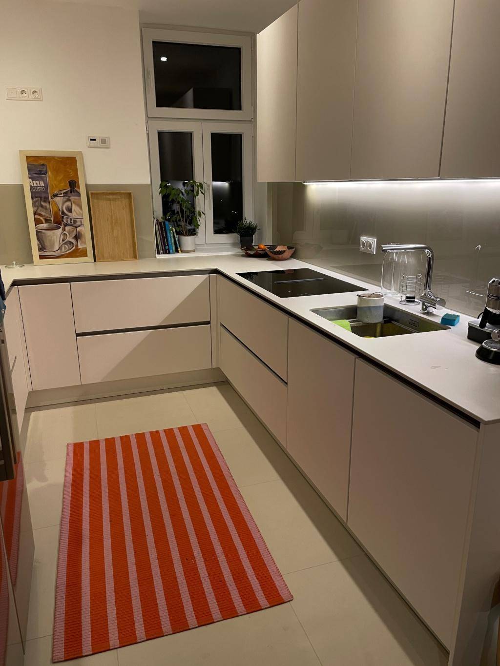 Moderne Küche mit hellen Schränken, integrierter Spüle und Fenster, beleuchtet bei Nacht.