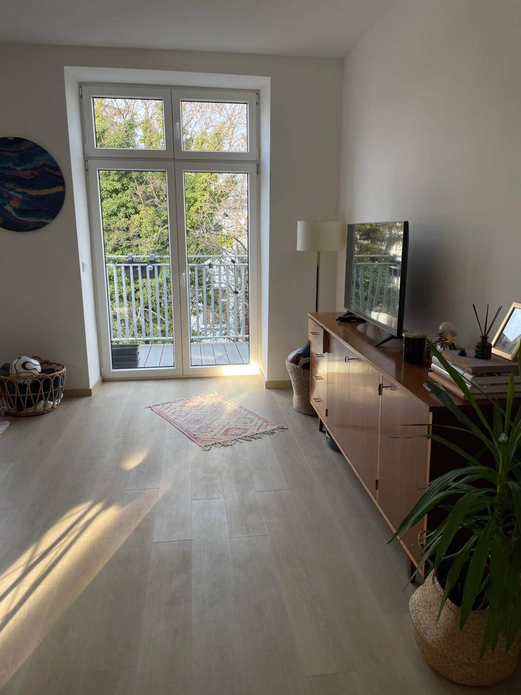 Helles Wohnzimmer mit Holzboden, Sideboard und Balkonzugang, sonnendurchflutet.