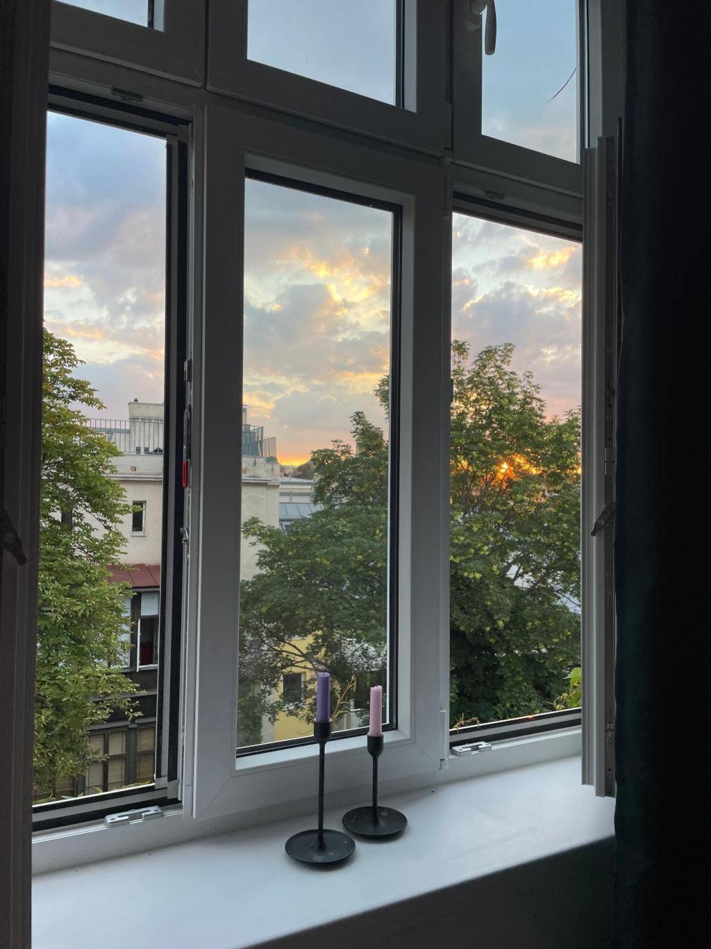 Fenster mit Blick auf den Sonnenuntergang über den Dächern und Bäumen der Stadt.