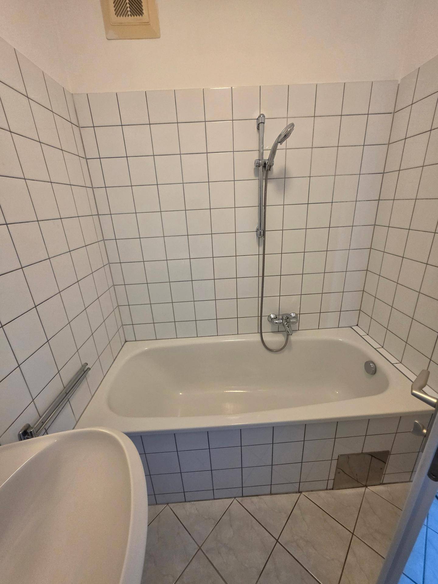 Gefliestes Badezimmer mit Badewanne und Duscharmatur, in einem funktionalen Stil.