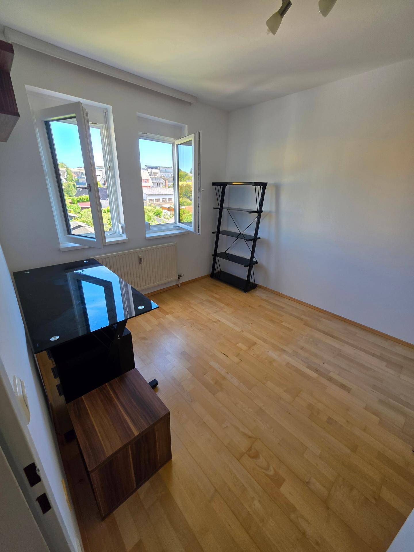 Helles Arbeitszimmer mit Holzboden, einem schwarzen Schreibtisch und Blick ins Grüne.