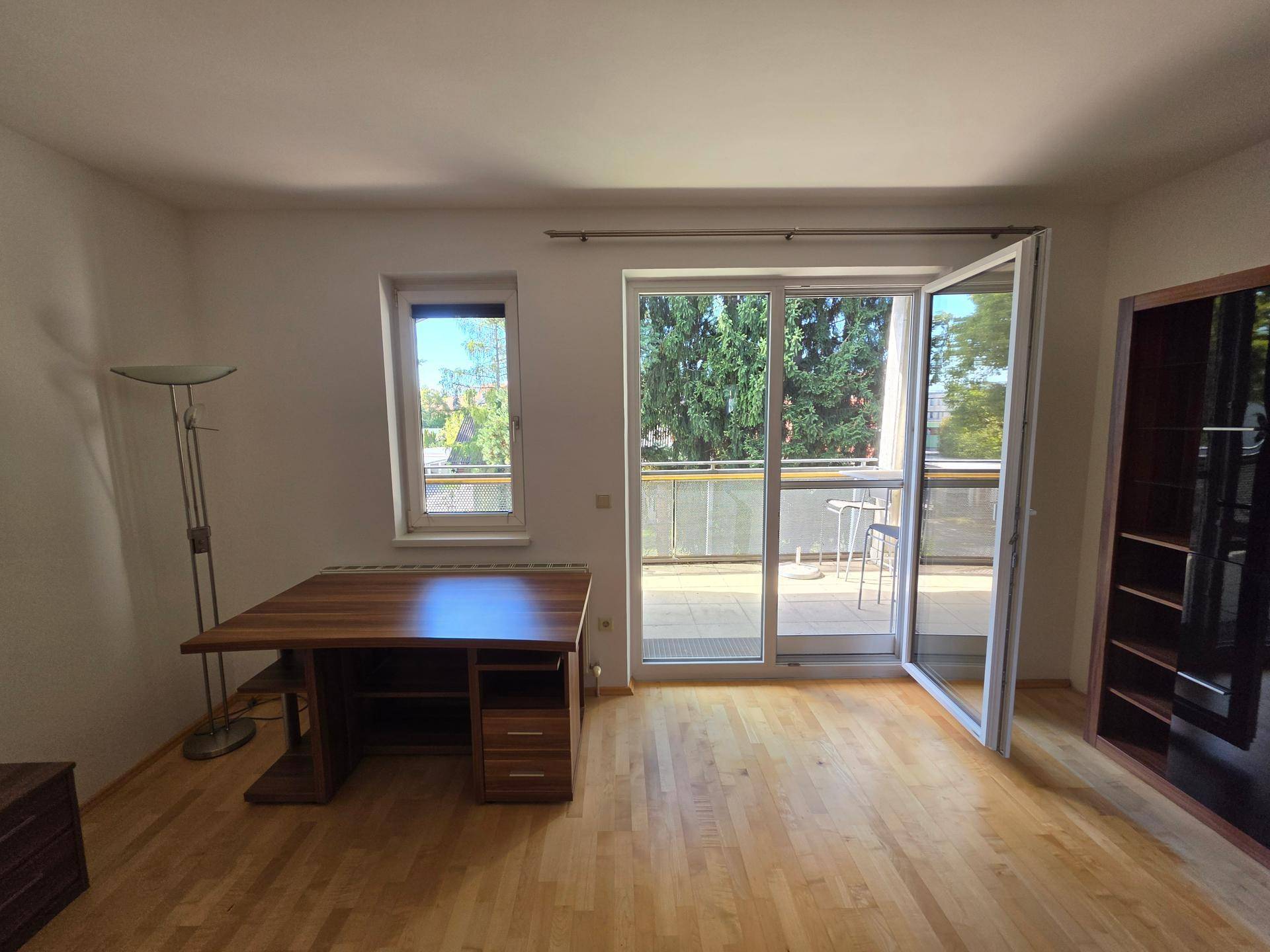 Geräumiger Raum mit Holzboden, Schreibtisch und direktem Zugang zu einem Balkon.