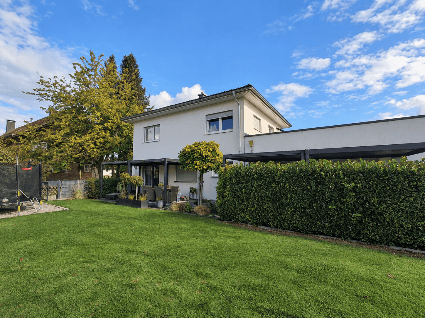 Großer Garten mit Rasenfläche, Trampolin und Blick auf das Einfamilienhaus.