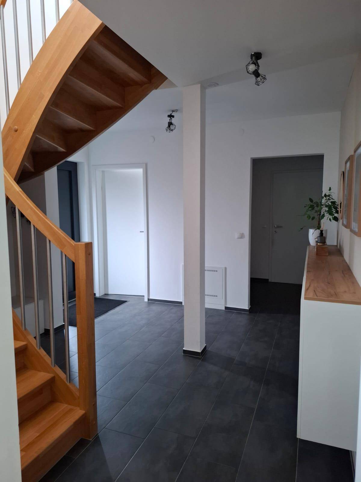 Geräumiger Flur mit Holztreppe, dunklem Fliesenboden und weißer Garderobe.