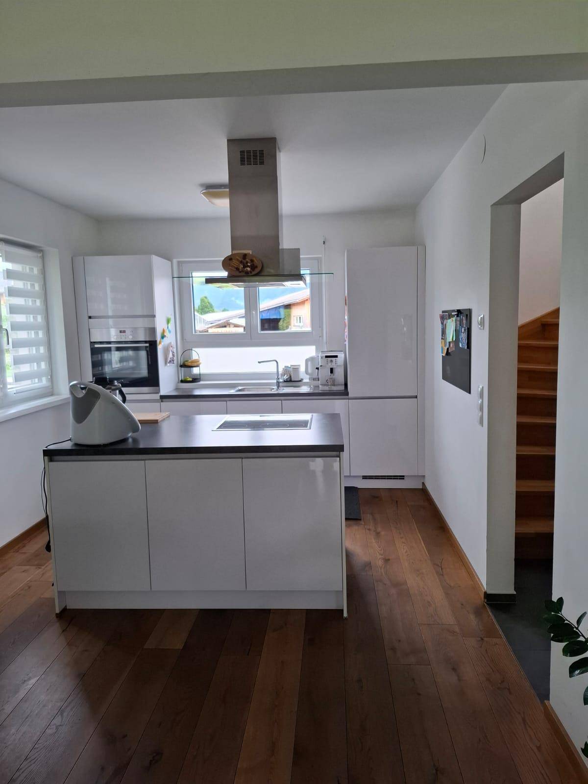 Moderne Küche mit Kochinsel, weißen Hochglanzfronten und Holzboden.