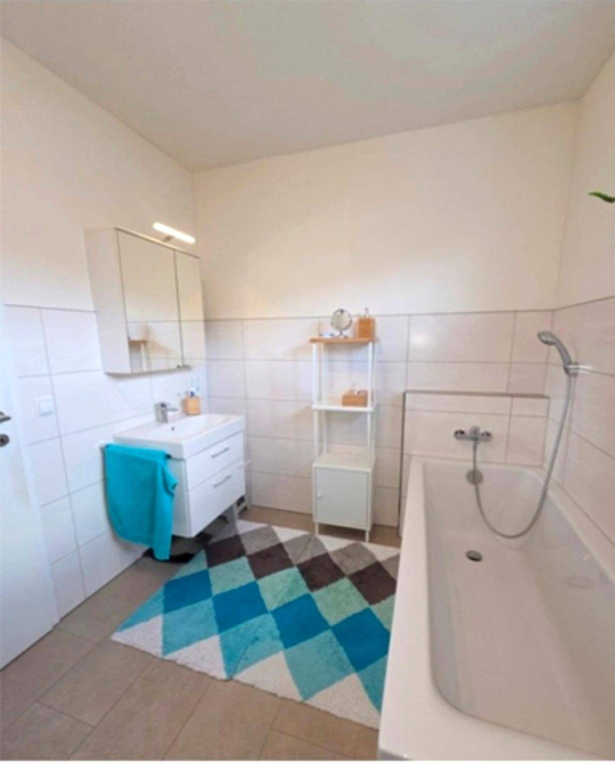 Helles Badezimmer mit Badewanne, Einzelwaschbecken und weißen Fliesen.
