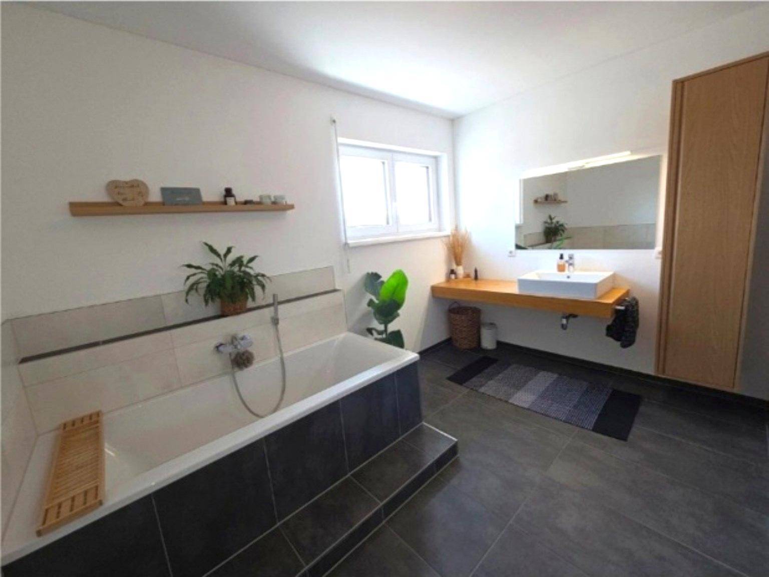 Modernes Badezimmer mit Badewanne, Einzelwaschbecken und dunklen Fliesen.