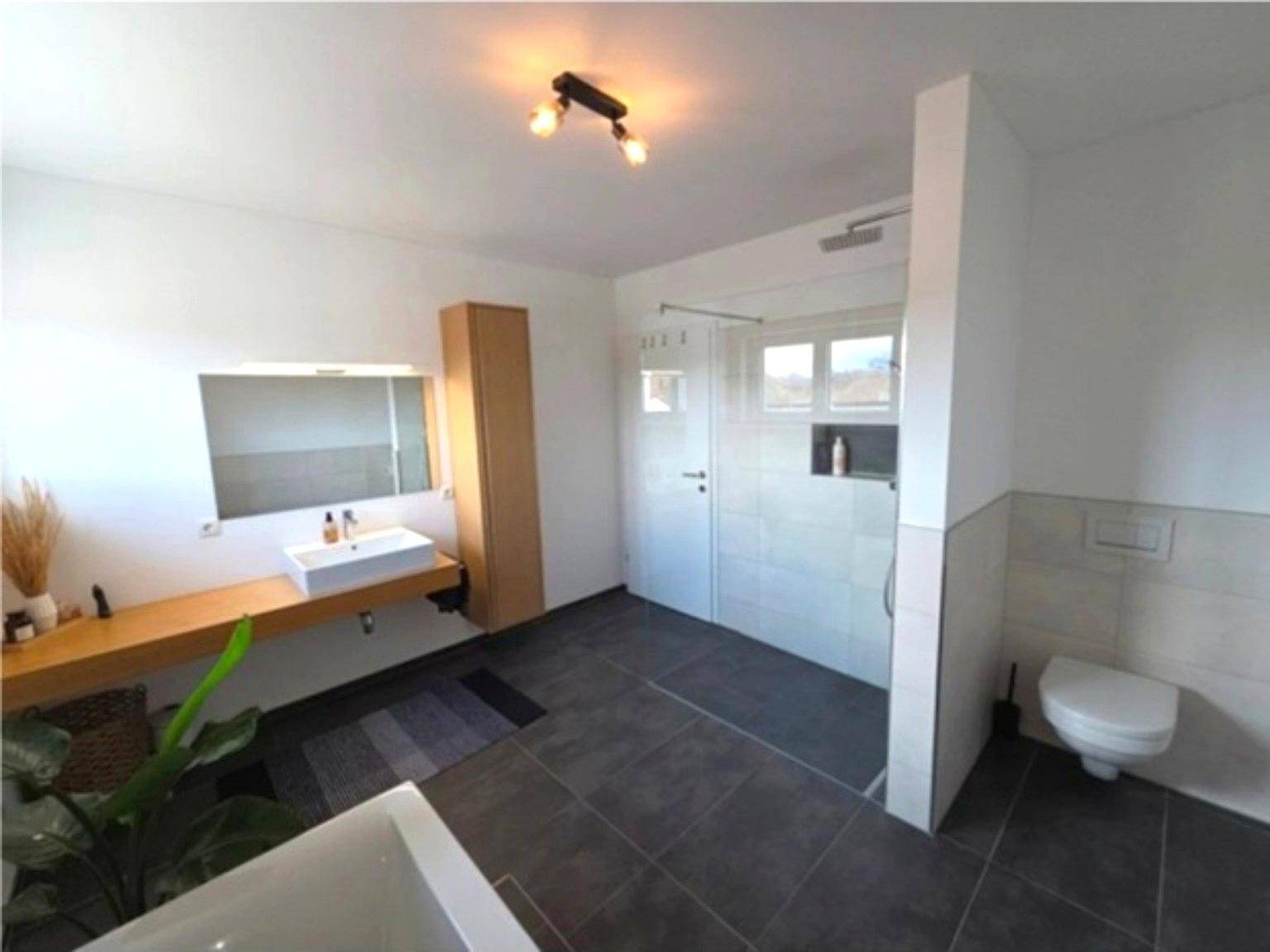 Geräumiges Badezimmer mit ebenerdiger Dusche, WC und modernem Design.