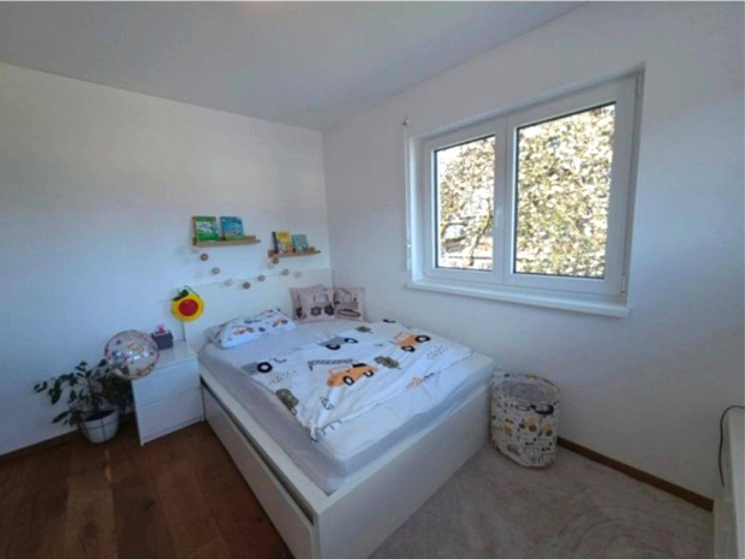 Kinderzimmer mit Holzboden, Einzelbett und hellem Fenster.