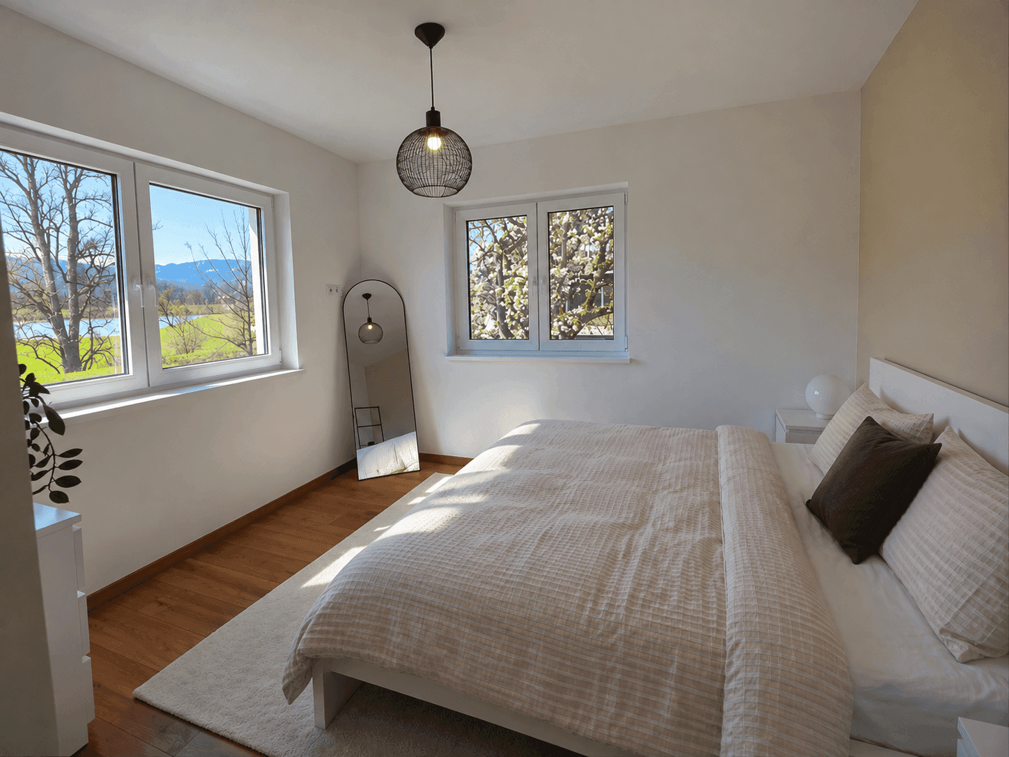 Helles Schlafzimmer mit Holzboden, Doppelbett und weitem Blick ins Grüne.