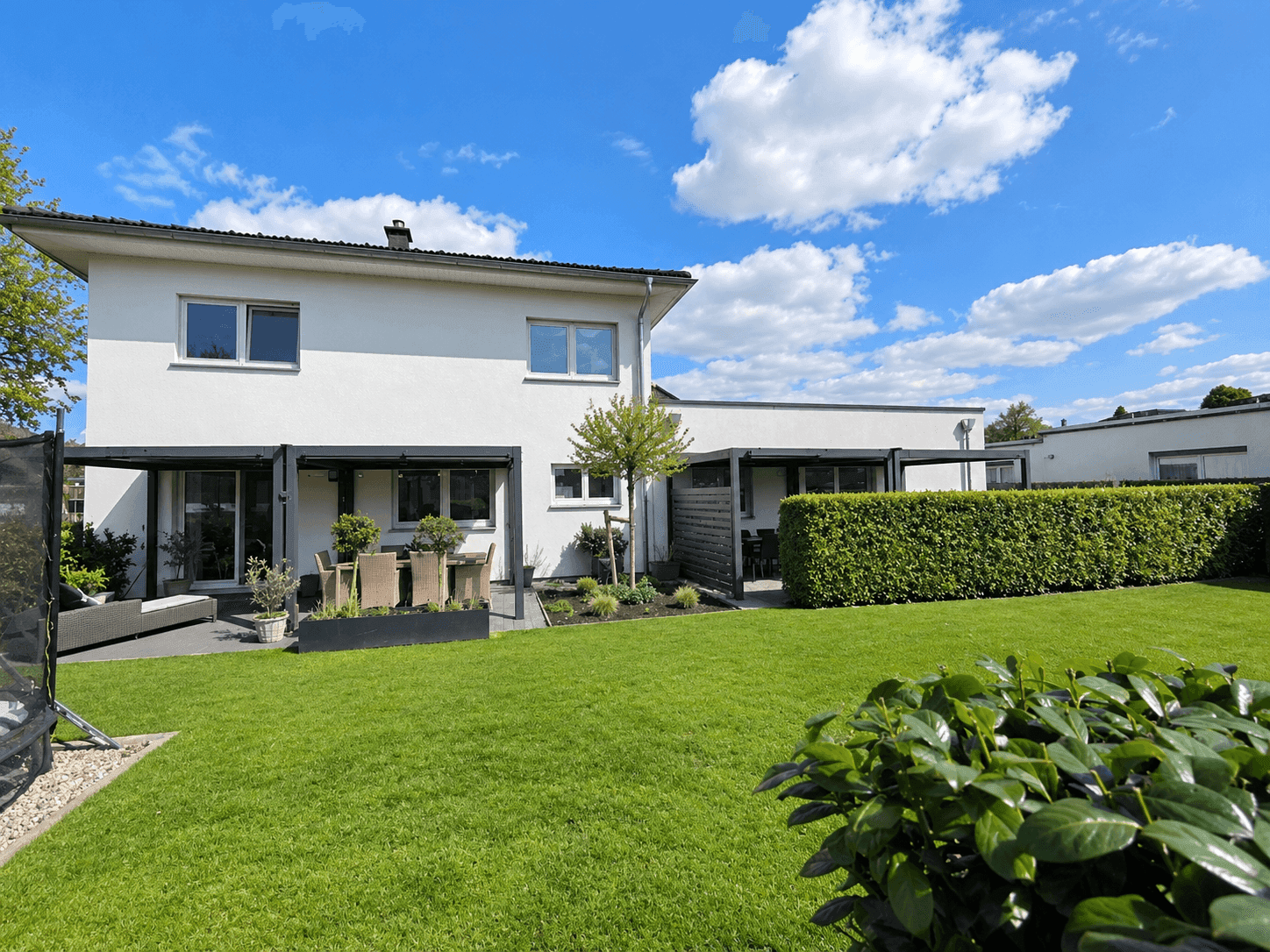 Weitläufiger Gartenbereich mit Rasen, Hecke und Terrasse am modernen Haus.