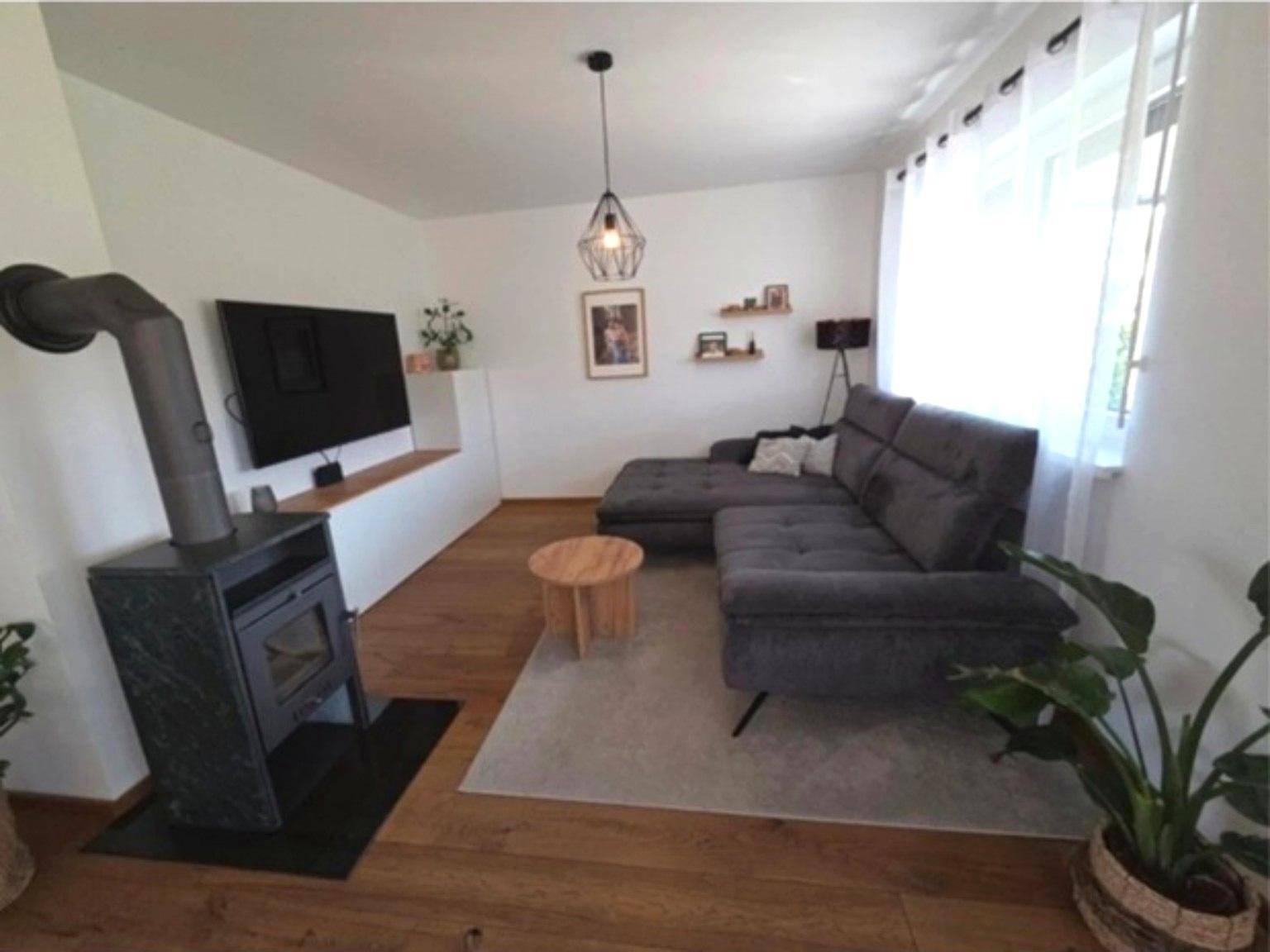 Gemütliches Wohnzimmer mit Kaminofen, großem Sofa und Holzboden.