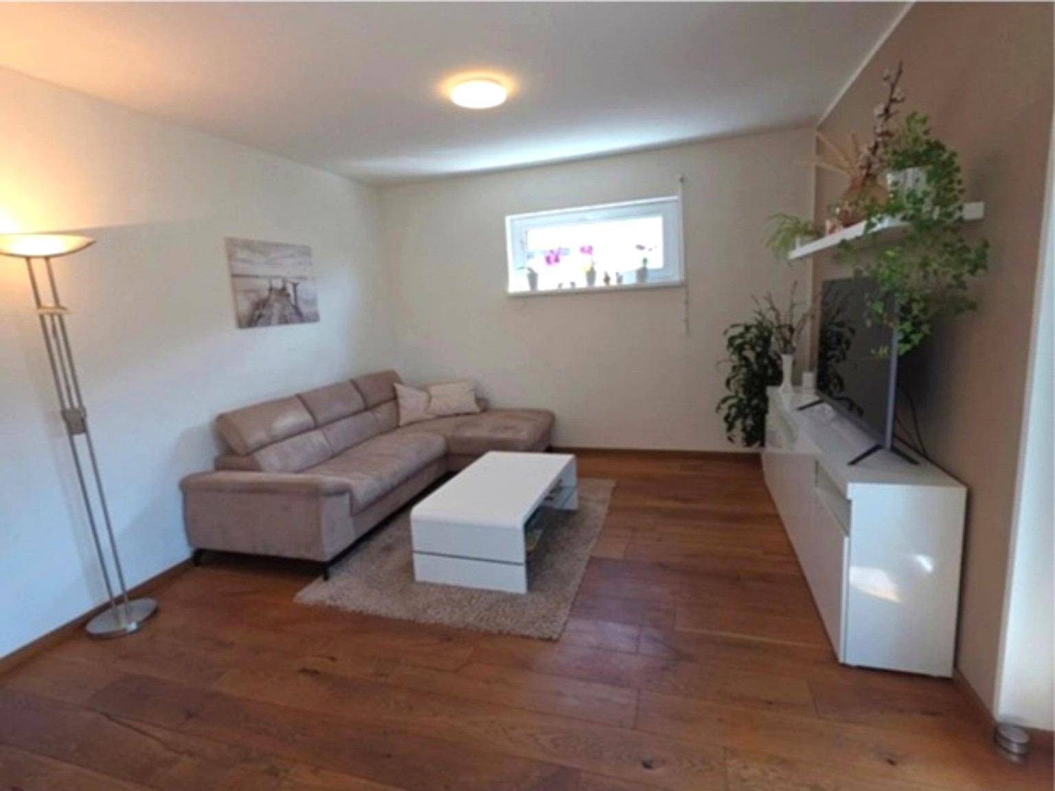 Gemütliches Wohnzimmer mit hellem Sofa, TV-Möbel und Holzboden.