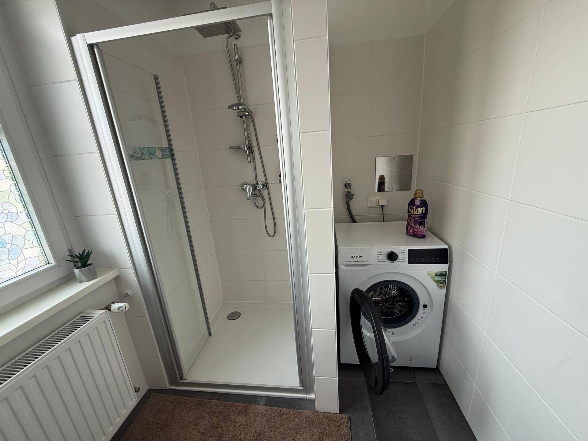 Modernes Badezimmer mit Duschkabine und integrierter Waschmaschine.