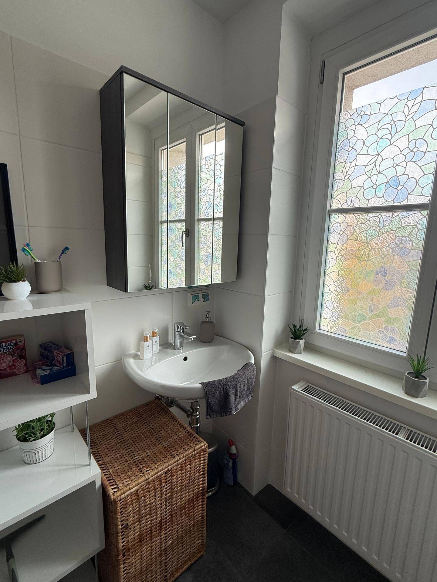 Badezimmer mit Waschbecken, Spiegelschrank und Fenster mit dekorativer Folie.