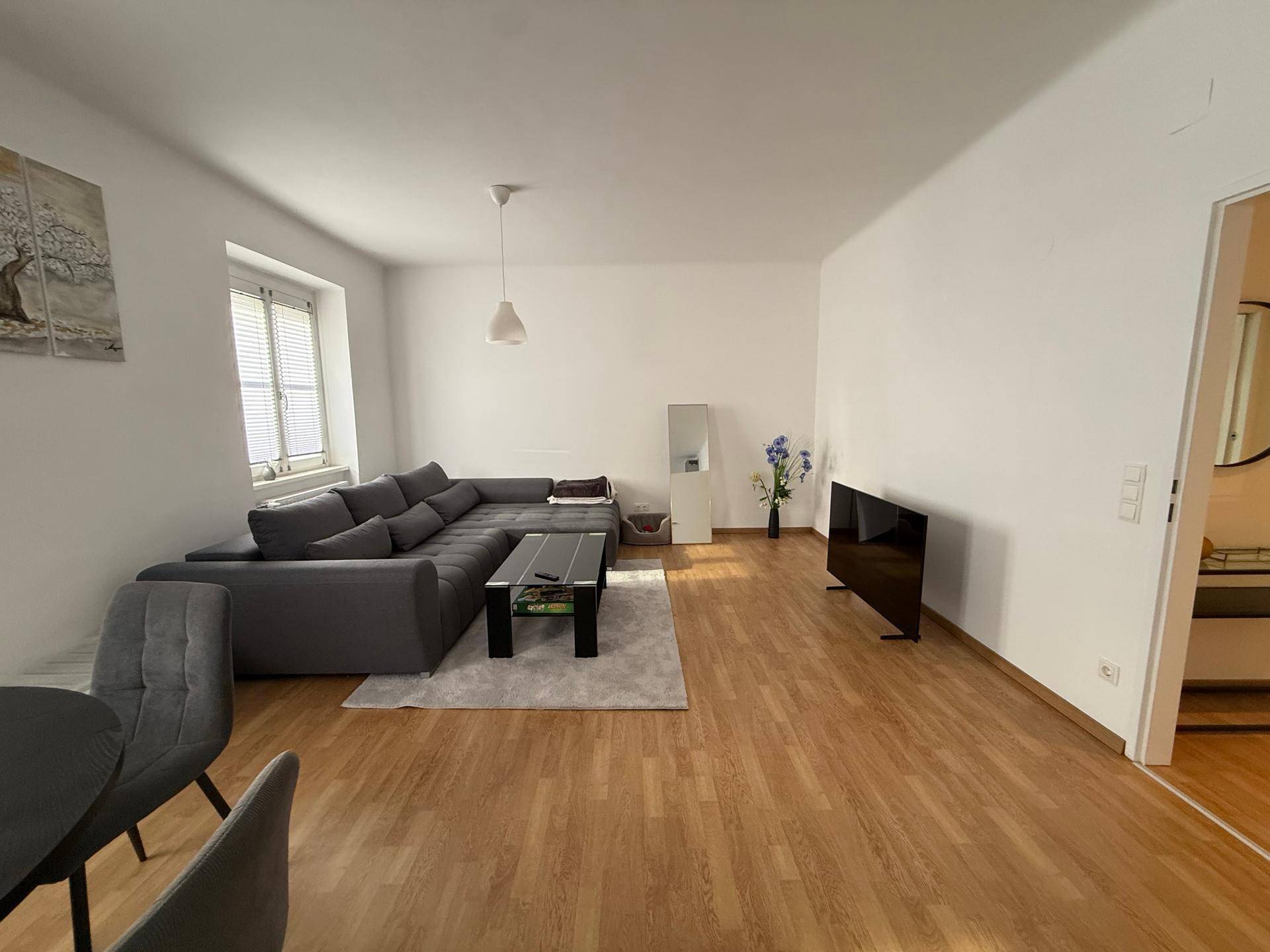Heller Wohn- und Essbereich mit Sofa, Esstisch und Parkettboden.